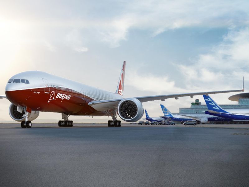 One red-colored jet aircraft with Boeing markings on an airport ramp, with three others in blue parked at gates.