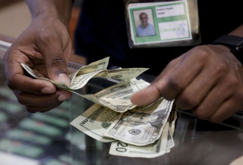 Cashier Andrew Powers completes a cash marijuana purchase at Cannabis City during the first day of legal retail marijuana sales in Seattle, Washington July 8, 2014. Washington became the second U.S. state to allow the sale of marijuana for recreational use on Tuesday, although shortages and high prices are likely to accompany any euphoria. Shops started to open on Tuesday, a day after 25 outlets were issued licenses under a heavily regulated and taxed system approved by voters in November 2012. REUTERS/Jason Redmond (UNITED STATES - Tags: SOCIETY DRUGS BUSINESS)