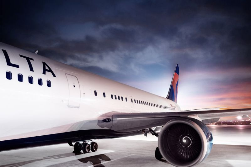 Delta-labeled aircraft on white flooring under a dark sky near sunset.