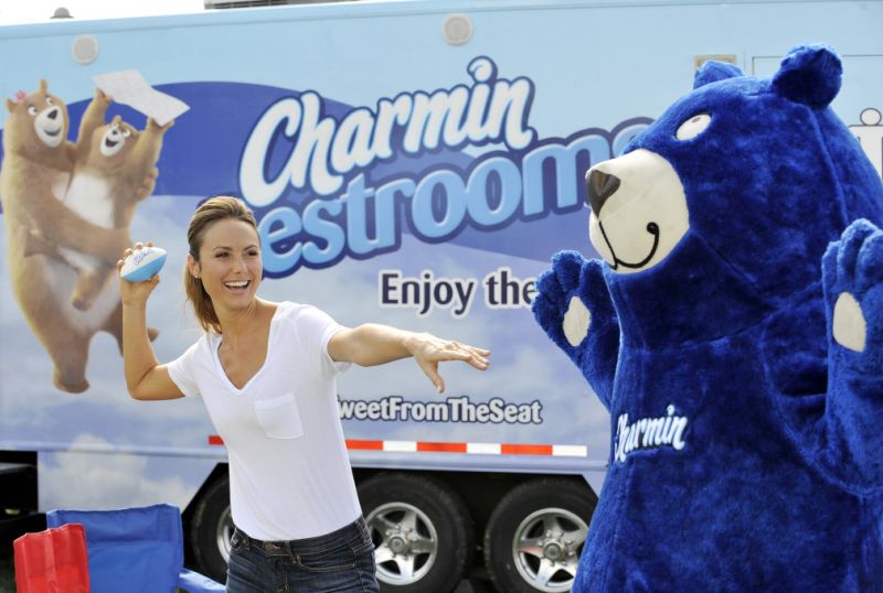 Woman throwing small football in front of a blue bear mascot, with semitrailer in background displaying a Charmin ad