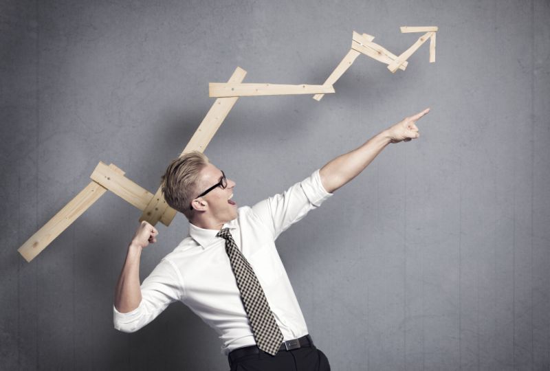 Man in white dress shirt and tie celebrating in front of a wooden arrow chart indicating gains.