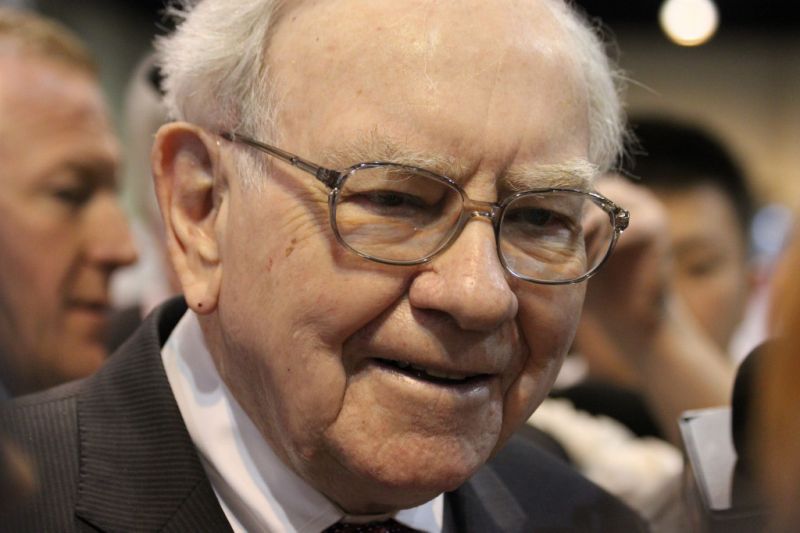 Warren Buffett smiling with a crowd of people behind him.