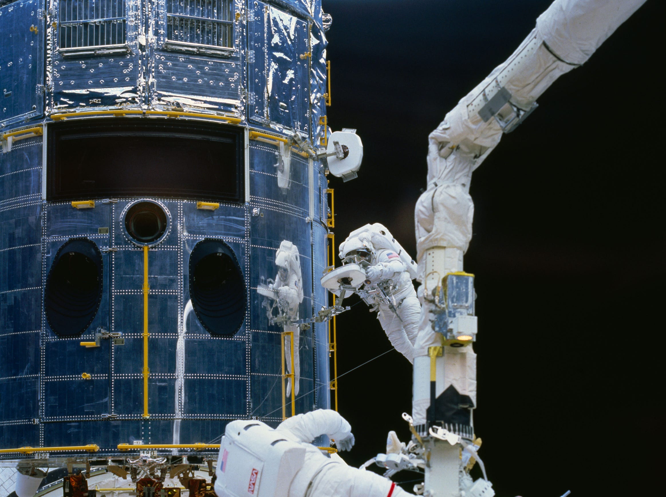 Astronaut F. Story Musgrave (top right center) works with a restraint device, on Dec. 5, 1993 near the Hubble Space Telescope (HST) during the first of five STS-61 extravehicular activities (EVA). Astronaut Jeffrey A. Hoffman, who joined Musgrave for three of the five spacewalks, is seen at the bottom of the frame preparing to work with fuse plugs.