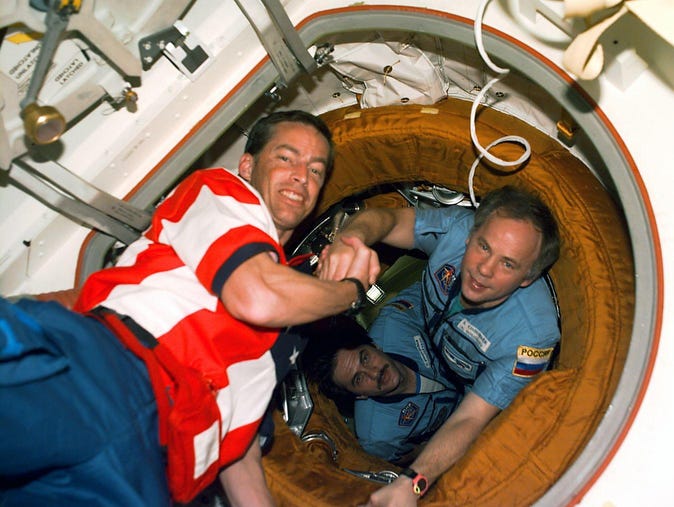 US Space Shuttle Atlantis Commander James Wetherbee (L) shakes hands with the Russian Space Station Mir 24 Commander Anatoly Slolovyev on Sept. 27 1997, in the vestibule of Mir's docking module as Mir 24 Flight Engineer Russian Pavel Vinogradov (C) looks on shortly after hatch opening. Atlantis and her crew of seven are on the seventh Mir/Shuttle docking mission..