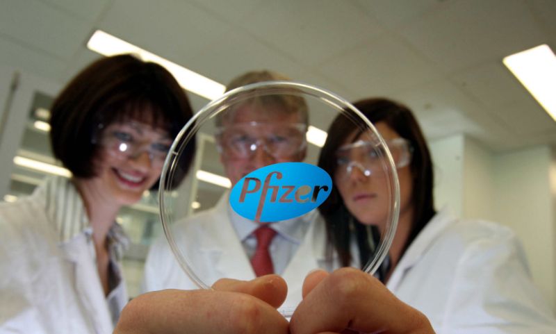 Three people in white coats looking at a Pfizer petri dish.