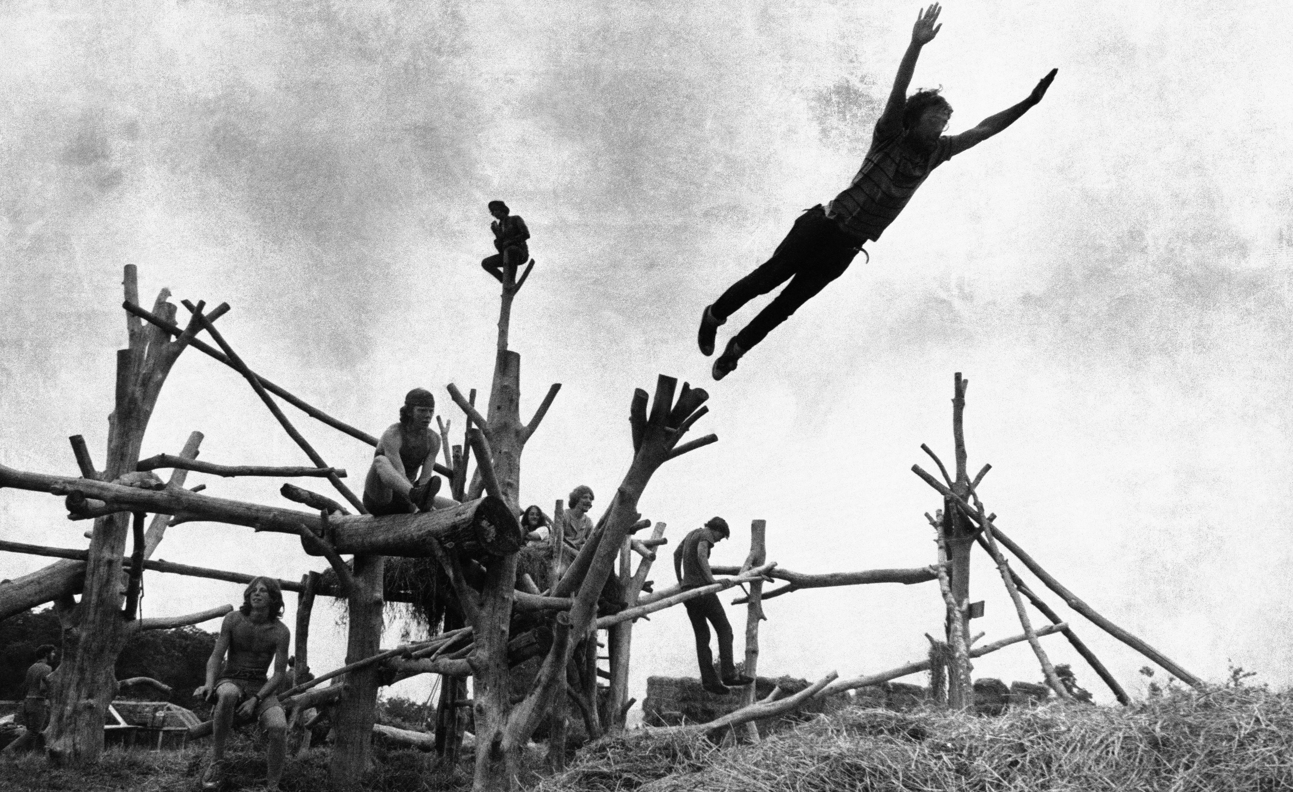 Rock music fans sit on a tree sculpture as one leaps mid-air onto a pile of hay during the Woodstock Music and Art Festival held on a cow pasture at White Lake in Bethel, New York on Aug. 15, 1969.