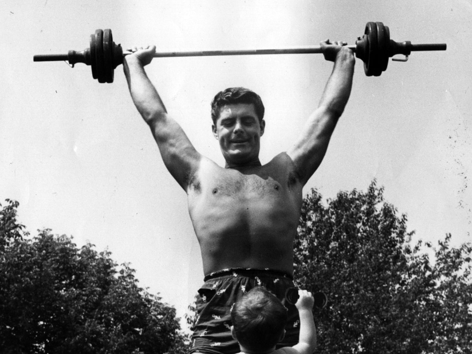 Entertainer Bob Braun, a former weightlifter at Baker&#39;s Gym and a Coney Island life guard, lifts barbells over his head while his son, Rob, watches in their North College Hill backyard on Oct. 5, 1958.&nbsp;