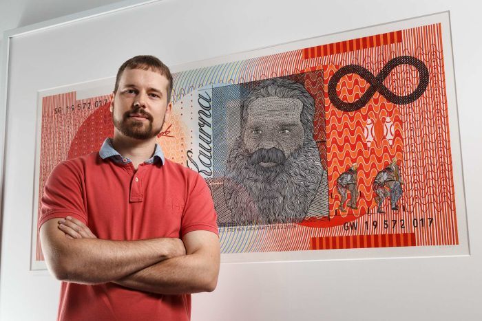 presley in a red shirt, arms crossed in front of his painting of the orange $20 note.