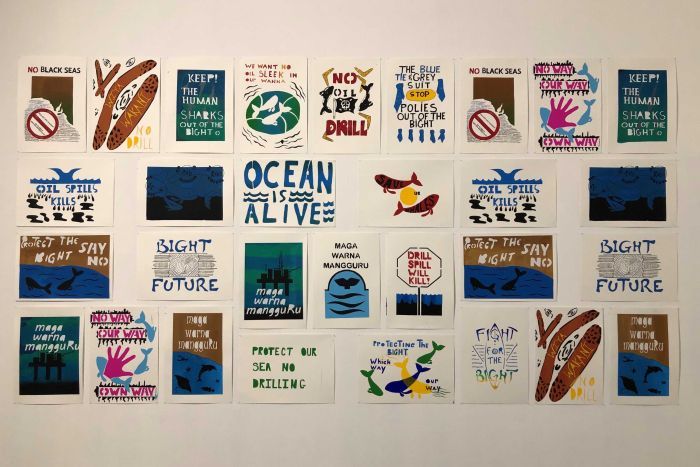 20 prints adorn a white wall with various slogans such as 'ocean is alive' and 'oil spill kills'