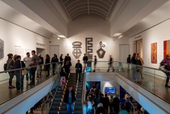 A shot of the gallery and artwork, with people milling about and walking up the stairs