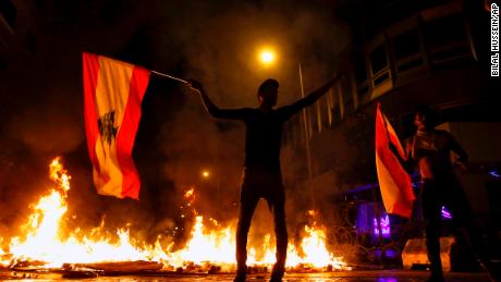 An anti-government protester holds a Lebanese flag in front of a barricade on fire on a road leading to the parliament building, during ongoing protests against the government, in Beirut, Lebanon, Wednesday, Nov. 13, 2019. 