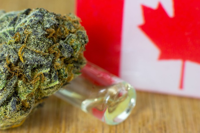 A cannabis bud and vial of cannabinoid-rich liquid next to a small Canadian flag.