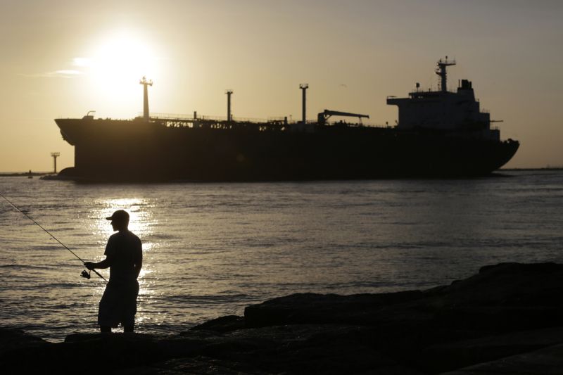 FILE - In this July 21, 2015, file photo, an oil tanker passes a fisherman as it enters a channel near Port Aransas, Texas, heading for the Port of Corpus Christi. The U.S., seemingly awash in crude oil after an energy boom sent thousands of workers scurrying to the plains of Texas and North Dakota, will begin exporting oil for the first time since the 1973 oil embargo. (AP Photo/Eric Gay, File)