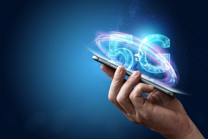 A hand holding a smartphone. 5G is written above the phone.