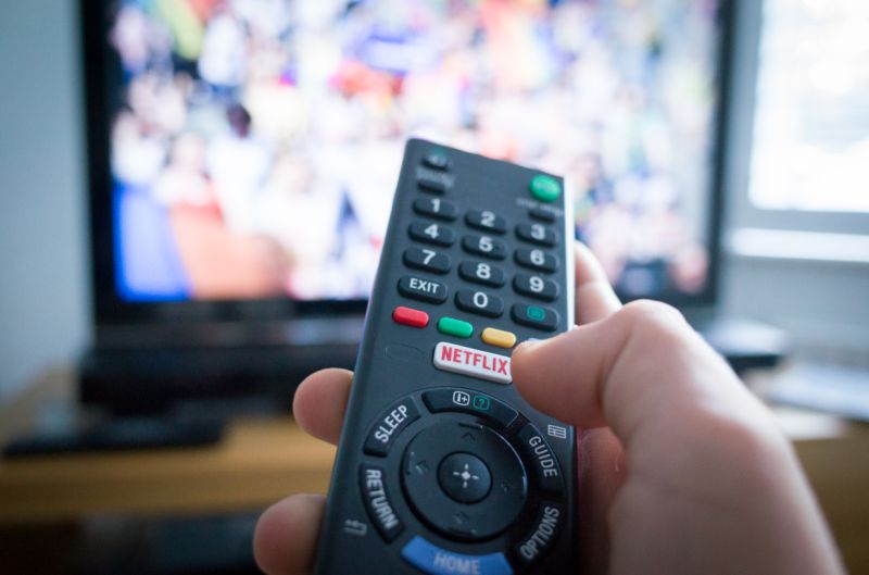 Southampton, England - July 31, 2017: Using a television remote control with dedicated Netflix button, TV in the background.