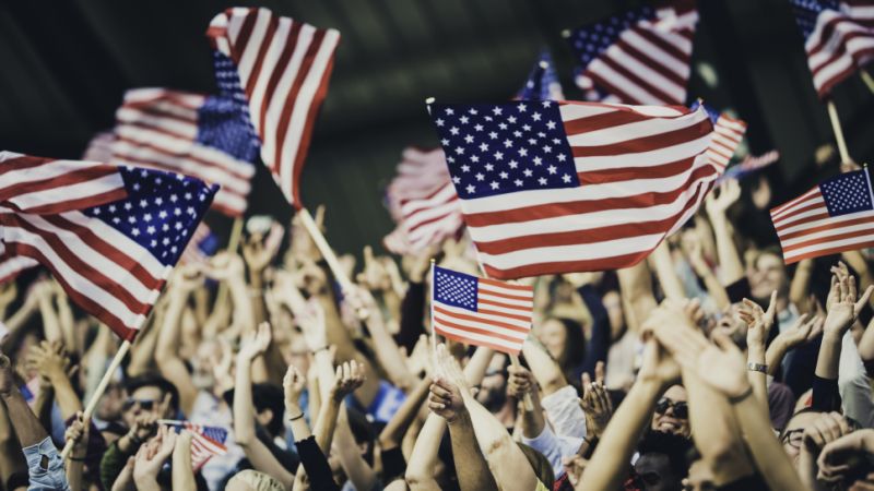 People with USA flags on a stadium cheering for their team during a sports event.