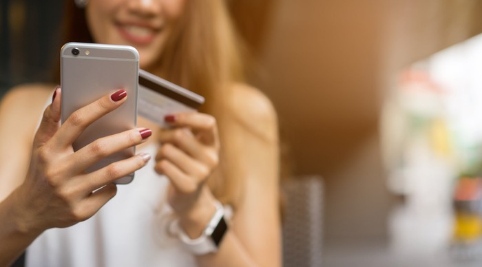 Smiling young woman holding an iPhone and a credit card