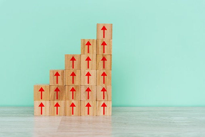 Wooden blocks with red up arrows on them are stacked in a stair-step fashion on a table near a wall.