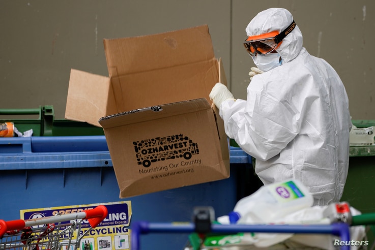 A worker dressed in personal protective equipment disposes of rubbish outside a public housing tower, reopened following a COVID-19 lockdown, in Melbourne