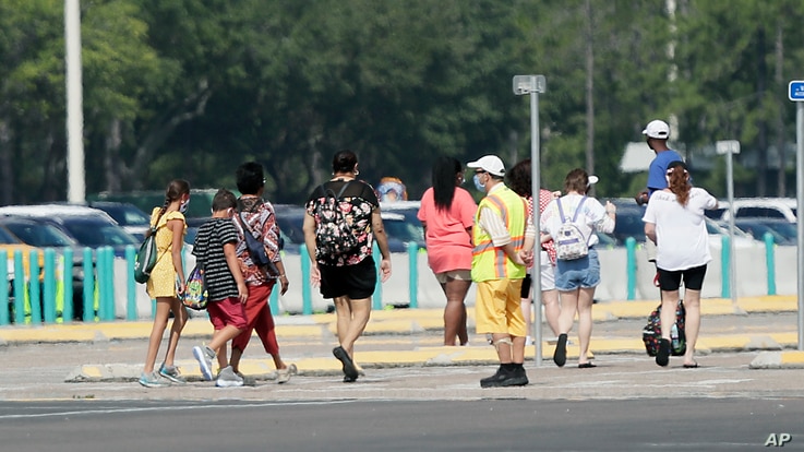 An attendant, front, directs park guests to the entrance of the Magic Kingdom during the reopening at Walt Disney World,…