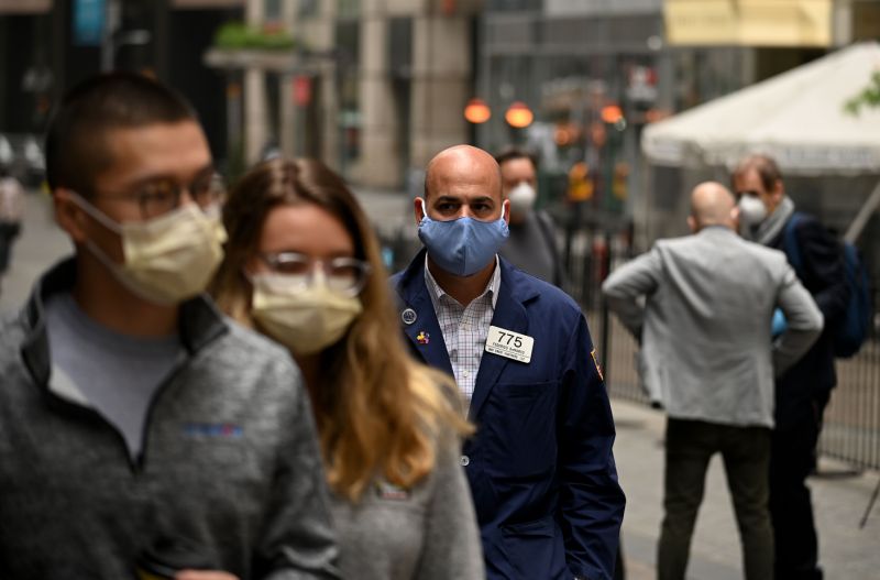 A trader walks in front of the New York Stock Exchange (NYSE) on May 26, 2020 at Wall Street in New York City. - Wall Street stocks surged early May 26, 2020 on optimism about coronavirus vaccines as the New York Stock Exchange resumed physical floor trading for the first time since late March. About five minutes into trading, the Dow Jones Industrial Average was up 2.3 percent at 25,023.76. The broad-based S&P 500 gained 2.0 percent to 3,013.04, while the tech-rich Nasdaq Composite Index advanced 1.6 percent to 9,468.96.The gains came after a ceremony presided over by New York Governor Andrew Cuomo, who wore a mask as he rung the opening bell to signal the start of the day for traders, also clad in masks and separated by plexiglas. (Photo by Johannes EISELE / AFP) (Photo by JOHANNES EISELE/AFP via Getty Images)