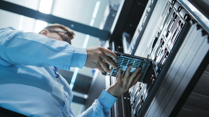 An engineer placing a hard drive into a server tower in a data center. 