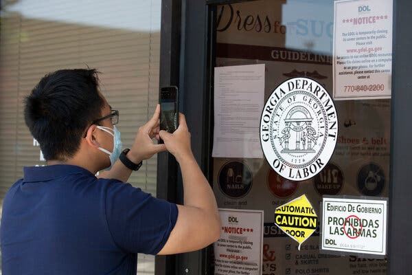 A copies phone numbers posted on the locked doors of a Georgia Department of Labor office. Fewer companies are recalling workers, even as federal aid as waned.